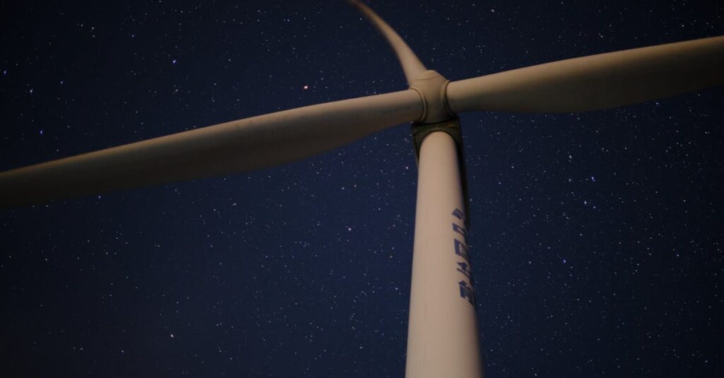 A low angle view of a wind turbine against a clear, star-filled night sky, symbolizing renewable energy.